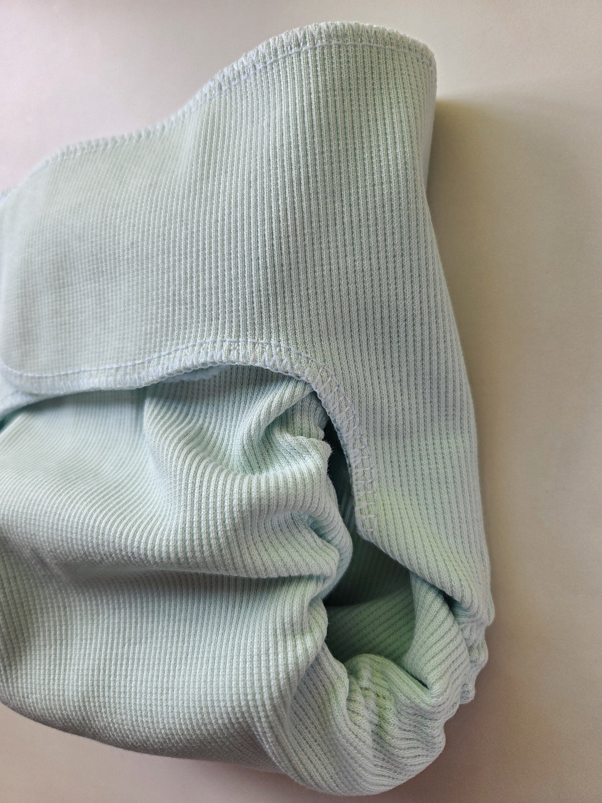 A close-up of a folded light mint green ribbed fabric cloth diaper or soft textile piece, shown on a plain light background.