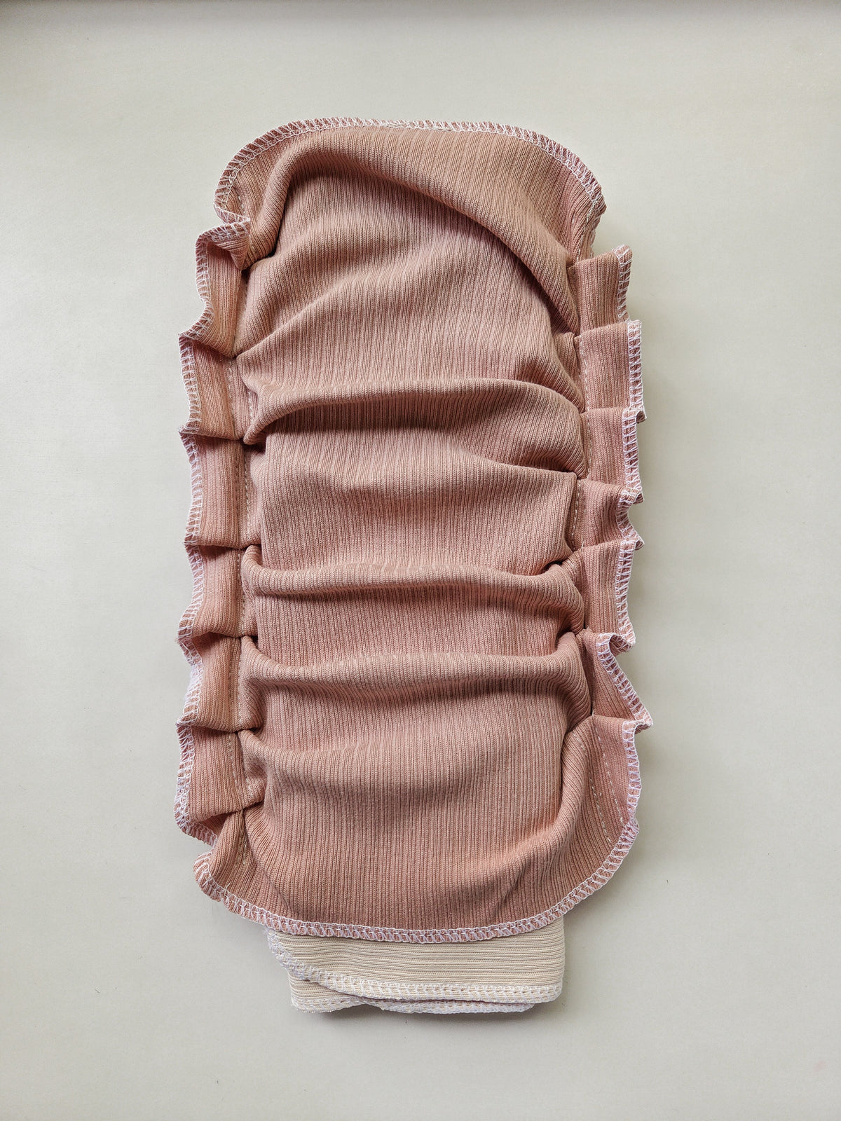 A dusty rose ribbed fabric reusable diaper with gathered pleats and a vanilla inner trifold for absorbency, shown flat on a light gray background.