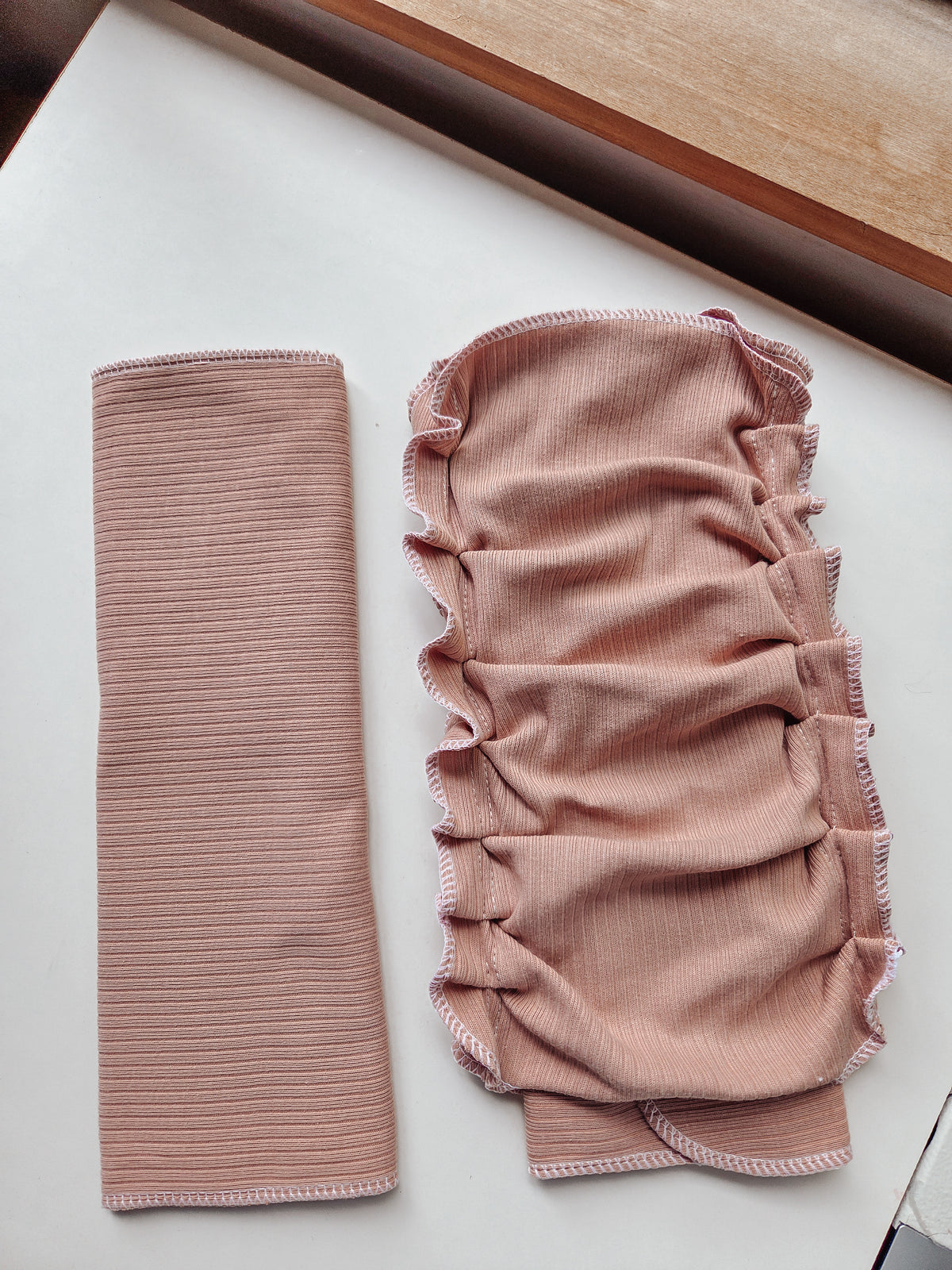 A dusty pink ribbed reusable diaper shown in two pieces on a white surface: a long narrow strip on the left and a gathered, ruched panel on the right with ruffled edges.